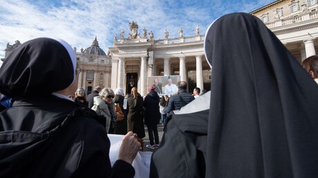 Menschen stehen auf dem Petersplatz und sehen sich das Mittagsgebet mit Papst Franziskus als Videoübertragung an, am 26. November 2023 im Vatikan / © Vatican Media/Romano Siciliani (KNA)