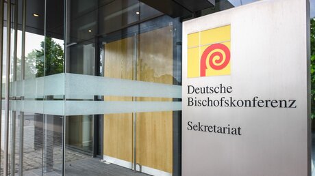 Logo der Deutschen Bischofskonferenz (DBK) auf einem Schild neben dem Eingang zum Sekretariat der DBK / © Elisabeth Schomaker (KNA)