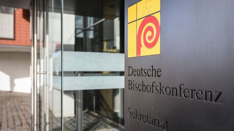 Logo der Deutschen Bischofskonferenz auf einem Schild neben dem Eingang zum Sekretariat der DBK / © Julia Steinbrecht (KNA)