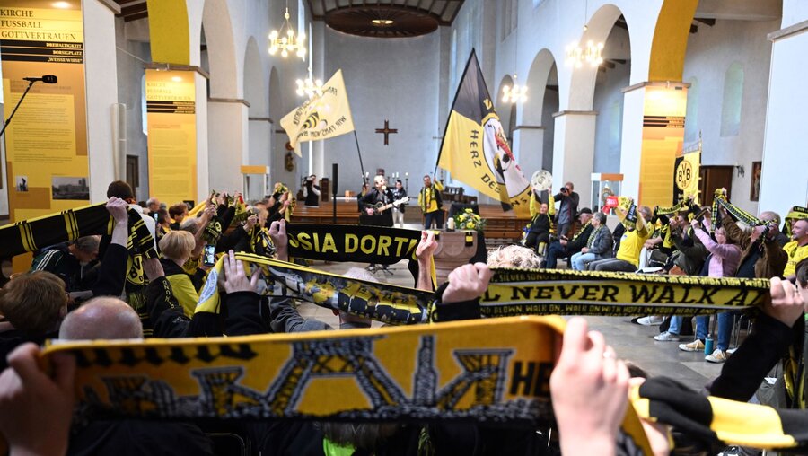 Fans von Borussia Dortmund halten beim Gottesdienst in der Gründungskirche des BVB ihre Fanschals in die Höhe / © Federico Gambarini (dpa)