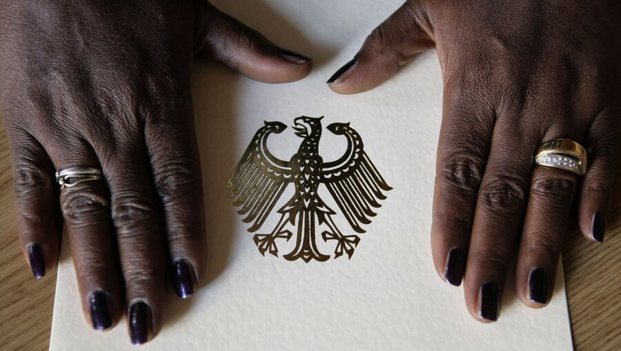 Die Hände einer Frau liegen auf der Einbürgerungsurkunde der Bundesrepublik Deutschland im Rathaus Berlin-Neukölln während einer Feierstunde zur Verleihung der deutschen Staatsbürgerschaft. / © Peer Grimm (dpa)
