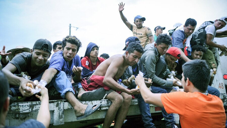 Migranten aus Mittelamerika sitzen auf der Ladefläche eines Fahrzeugs und werden von Passanten mit Nahrung versorgt, am 2. November 2018 bei Veracruz (Mexiko). / © Tobias Käufer (KNA)