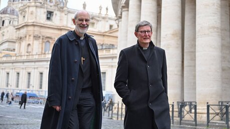Kardinal Rainer Maria Woelki (r.) und Weihbischof Ansgar Puff laufen an den Säulen der Petersplatzes entlang / © Johannes Neudecker (dpa)