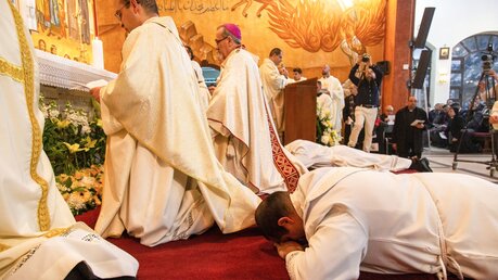 Geistliche beten und Weihekandidaten liegen auf dem Boden vor dem Altar bei der Priesterweihe am 12. Januar 2023 in Amman, Jordanien. / © Andrea Krogmann (KNA)