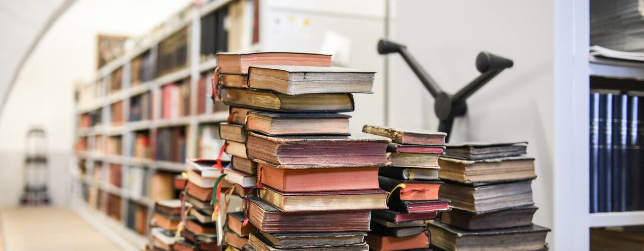 Alte Bücher liegen in Stapeln auf einem Tisch in einer Bibliothek / © Julia Steinbrecht (KNA)
