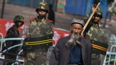 Ein Angehöriger der uigurischen Minderheit in China geht vorbei an chinesischen Sicherheitskräften / © Diego Azubel (dpa)