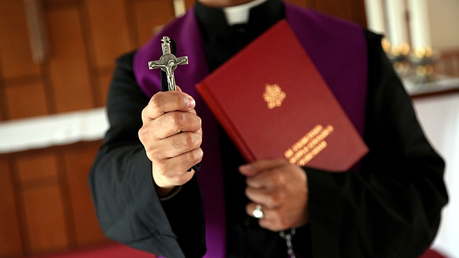 Priester mit Kreuz und Exorzismus-Handbuch / © Alexander Brüggemann (KNA)