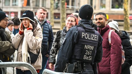 Ein Sicherheitsbeamter der Polizei spricht mit Touristen bei der Einlasskontrolle vor dem Hauptportal des Kölner Doms / © Harald Oppitz (KNA)