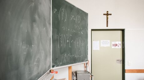 Eine Tafel ist mit mathematischen Formeln beschrieben in einem Klassenraum des katholischen Gymnasium Aloisiuskolleg in Bonn am 8. Juli 2019. Über der Tür hängt ein Kreuz. / © Julia Steinbrecht (KNA)