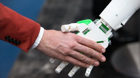 Ein humanoider Roboter gibt einem Menschen die Hand / © Friso Gentsch (dpa)