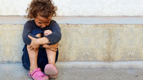 Ein Mädchen sitzt traurig auf dem Boden; Symbolfoto Kinderarmut Missbrauch / © Olesia Bilkei (shutterstock)