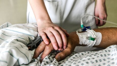 Hand einer Pflegerin liegt auf dem Handrücken eines Patienten auf einer Intensivstation / © Harald Oppitz (KNA)