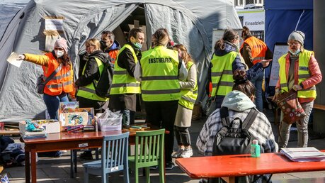 Freiwillige Helfer mit gelben und orangenen Warnwesten stehen am 11. März 2022 vor einem Zelt am Kölner Hauptbahnhof und erwarten Flüchtlinge aus der Ukraine. / © Adelaide Di Nunzio (KNA)