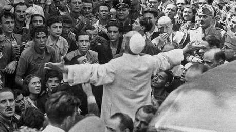 Papst Pius XII. spricht mit weit ausgebreiteten Armen am 13. August 1943 zu der Menschenmenge im römischen Stadtviertel Tuscolano, nach Beendigung der alliierten Bombardements auf die Stadt / © Osservatore Romano/Romano Siciliani/KNA (KNA)