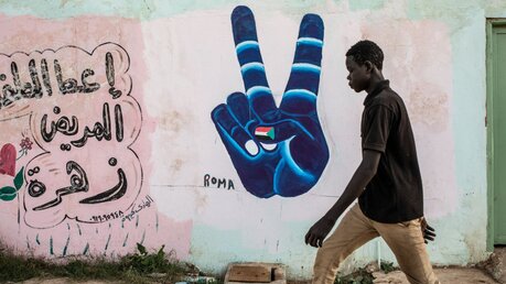 Ein Mann geht an einer Wand vorbei auf die das Zeichen der Revolution im Sudan gemalt ist / © Alessio Mamo (KNA)
