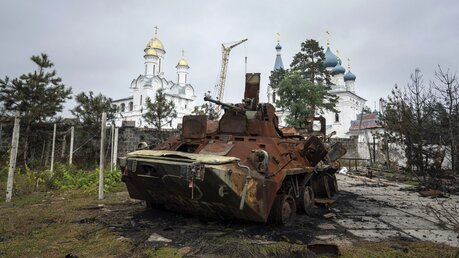 Isjum: Ein zerstörter russischer Schützenpanzer steht im Hof eines Ligusterhauses vor einer Kirche / © Evgeniy Maloletka (dpa)